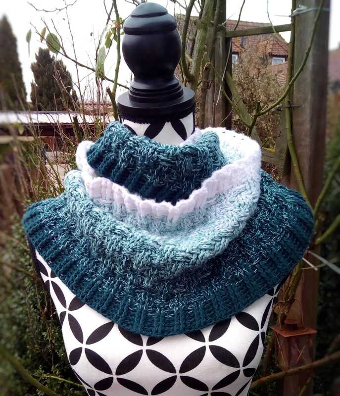 Dicker gehäkelter Loop-Schal in Petrol-, Türkis- und Weißtönen auf einer Schneiderbüste im Freien