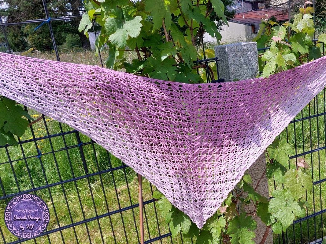Gehäkeltes Dreieckstuch in Rosé bis Lila mit offenem Muster an einem Gartenzaun