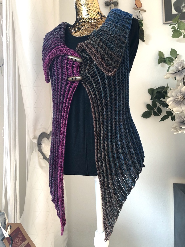 Gehäkelte Damenweste mit Farbverlauf in Magenta, Blau und Braun auf einer Schneiderpuppe, mit breitem Kragen und zwei Knebelknöpfen