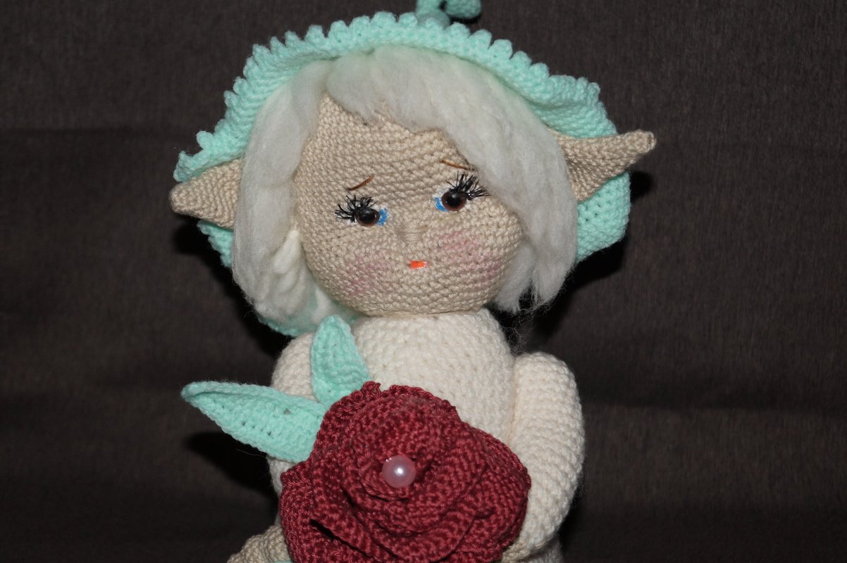 Gehäkelte Amigurumi‑Puppe mit Elfenohren hält rote Häkelrose