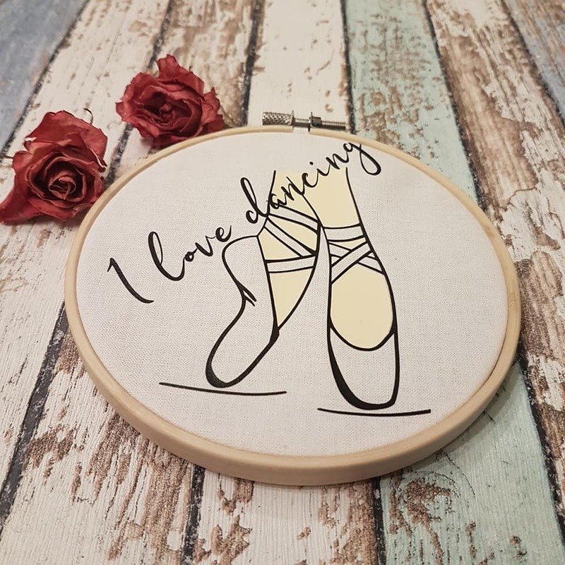 Stickrahmen mit Plottmotiv gekreuzter Ballett-Spitzenschuhe und dem Schriftzug 'I love dancing' auf rustikalem Holzhintergrund mit getrockneten roten Rosen