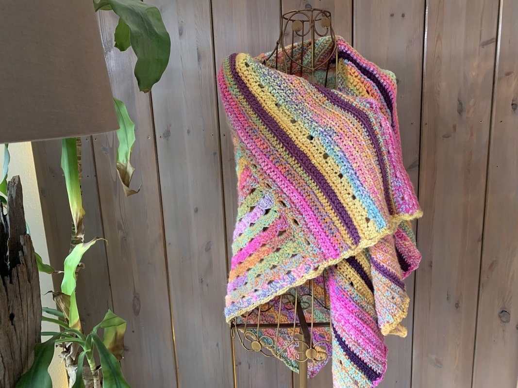 Mehrfarbiges gehäkeltes Dreieckstuch auf Schneiderpuppe mit Streifen- und Lochmustern in Pink, Gelb und Violett.