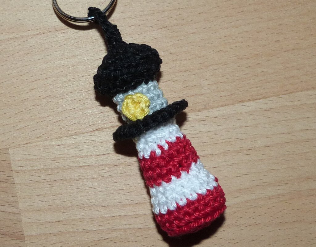 Gehäkelter Leuchtturm-Schlüsselanhänger in Rot, Weiß, Grau und Schwarz mit gelbem Detail auf Holz