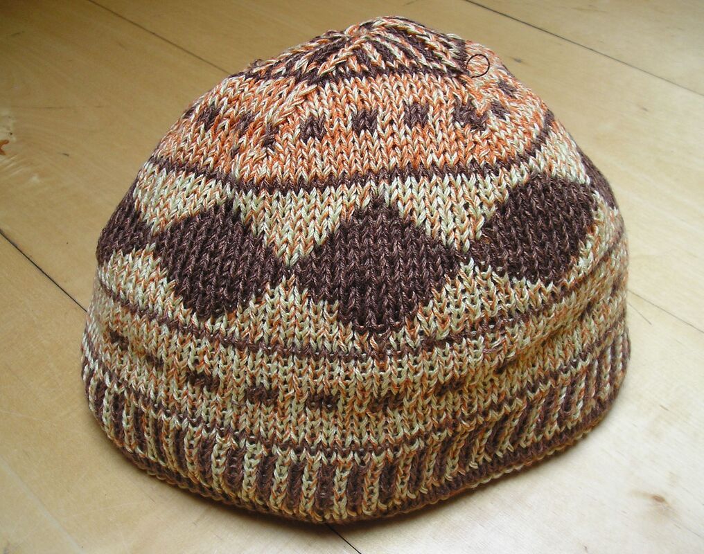 Gestrickte Mütze in Brauntönen mit mehrfarbigem Muster auf Holz
