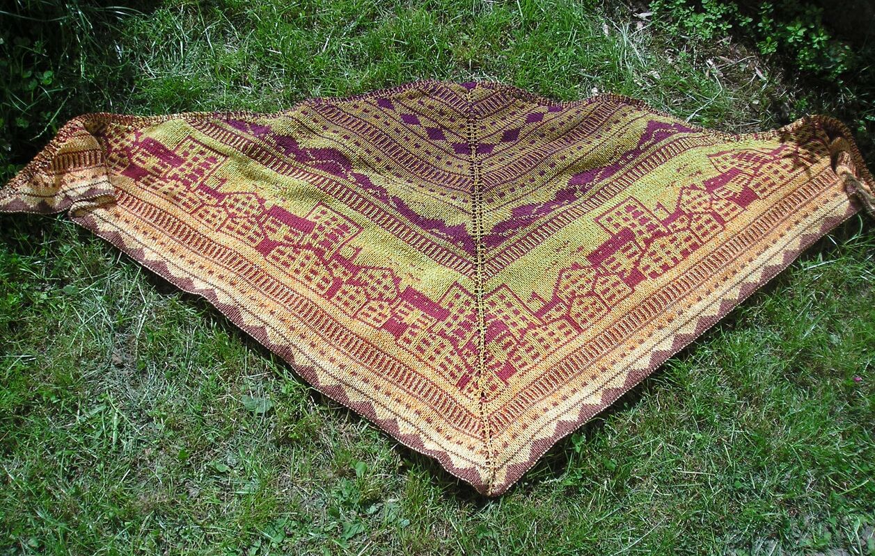 Dreieckstuch mit Häuser- und Streifenmustern in Gelb, Orange und Bordeaux auf grünem Rasen