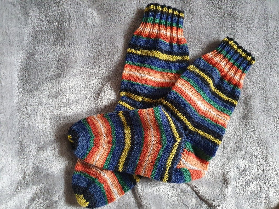 Ein Paar gestrickte Damensocken mit horizontalen Streifen in Blau, Orange, Gelb und Grün auf grauer Decke