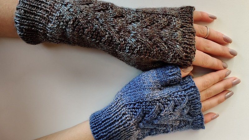 Zwei Hände mit gestrickten, fingerlosen Armstulpen mit Zopfmuster, eine braun-meliert, eine blau-meliert.