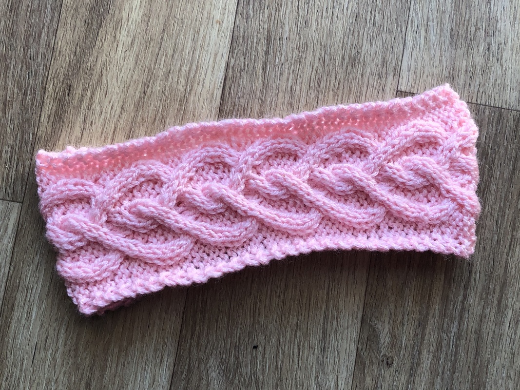 Rosa gestricktes Stirnband mit Zopfmuster auf Holz