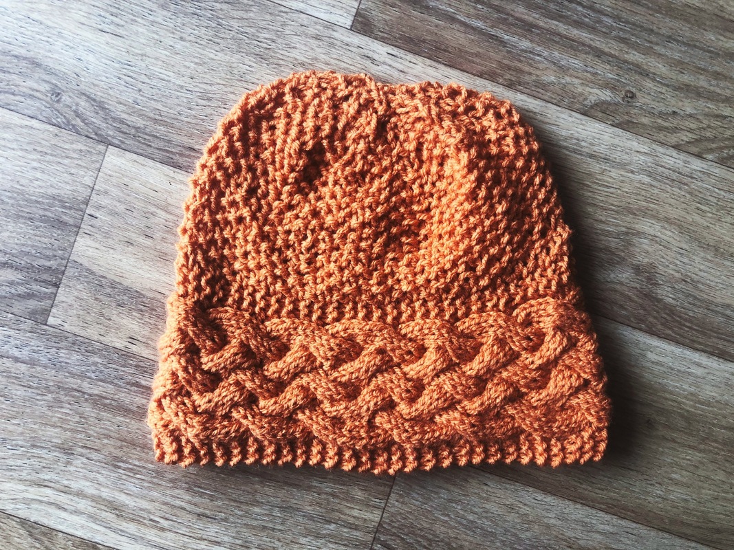 Orange Zopfmuster-Beanie flach auf Holz gelegt