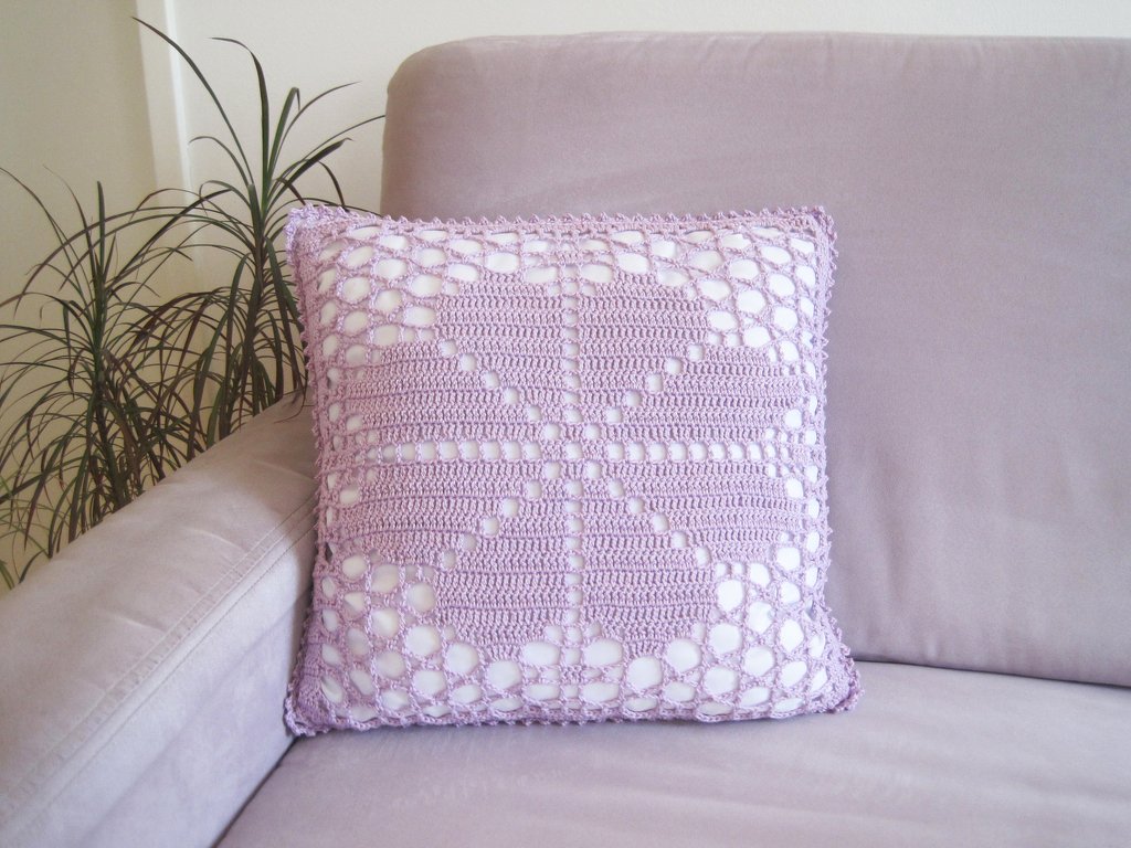 Quadratischer lilafarbener Kissenbezug mit gehäkeltem Herzmuster auf einem Sofa
