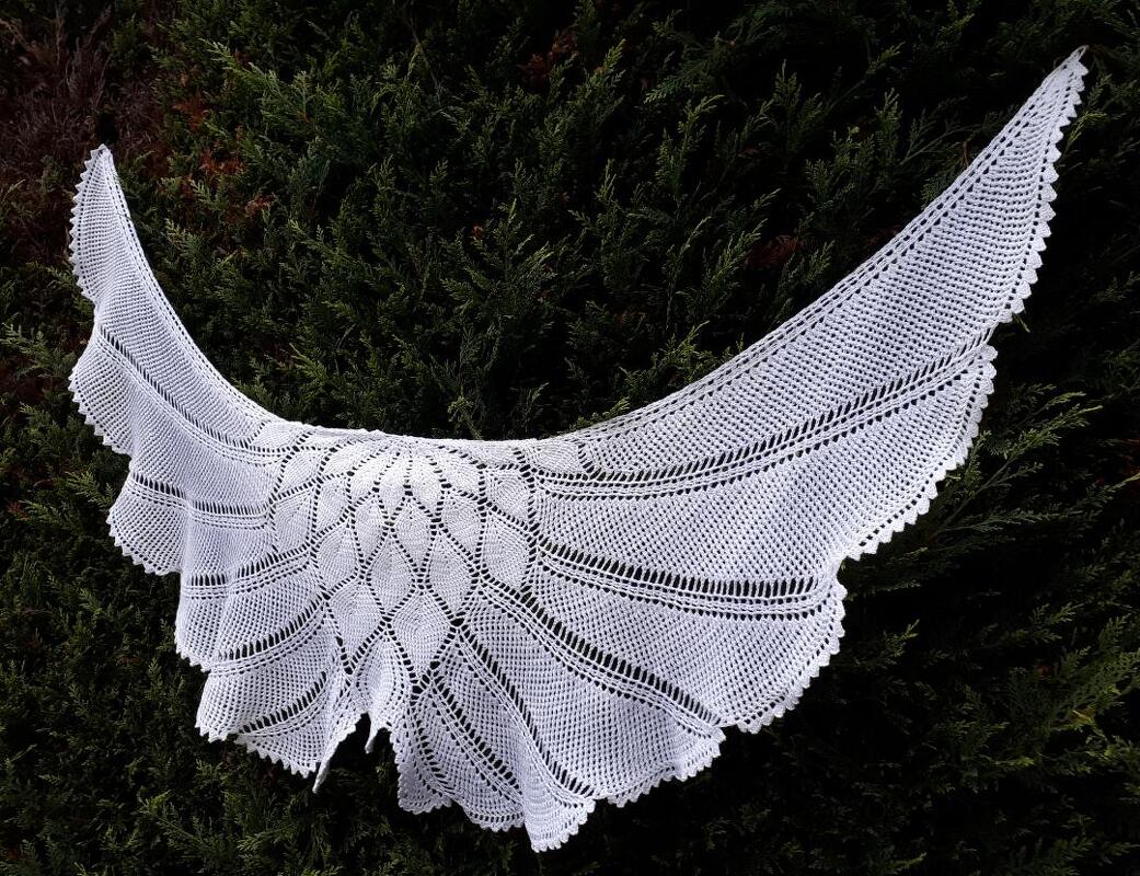 Weißes halbrundes Häkeltuch mit filigranem Spitzen- und Netzmuster vor dunkelgrünem Hintergrund.