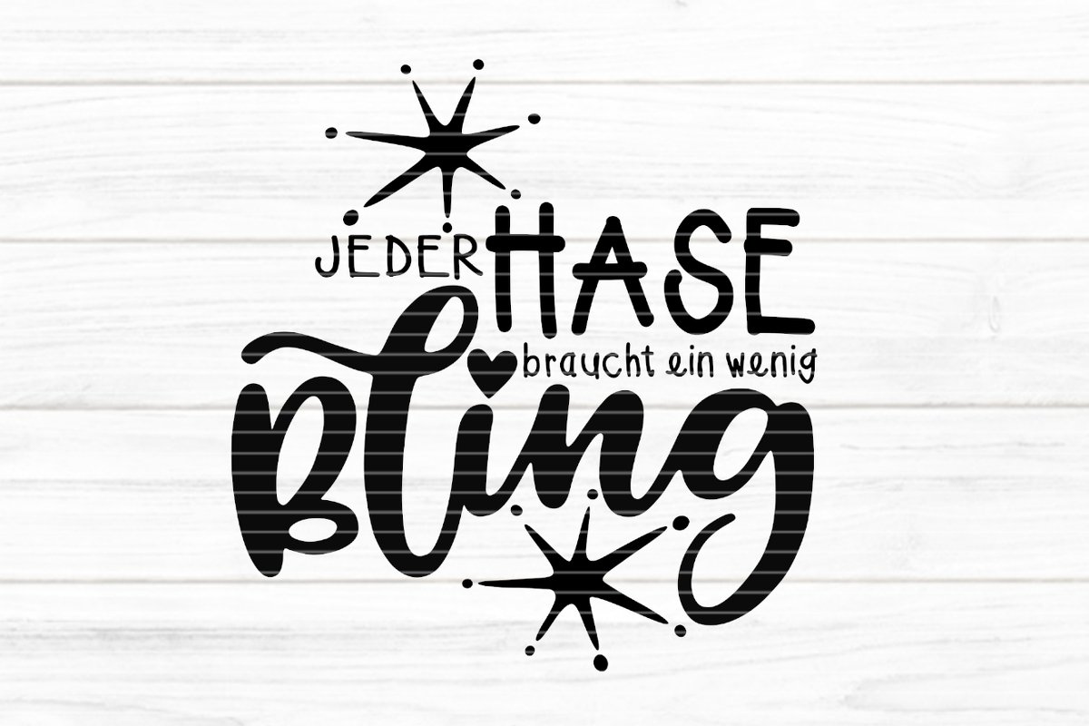Schwarzer Schriftzug „Jeder Hase braucht ein wenig Bling“ mit stilisierten Sternen und Herz auf hellem Holzbrett‑Hintergrund.