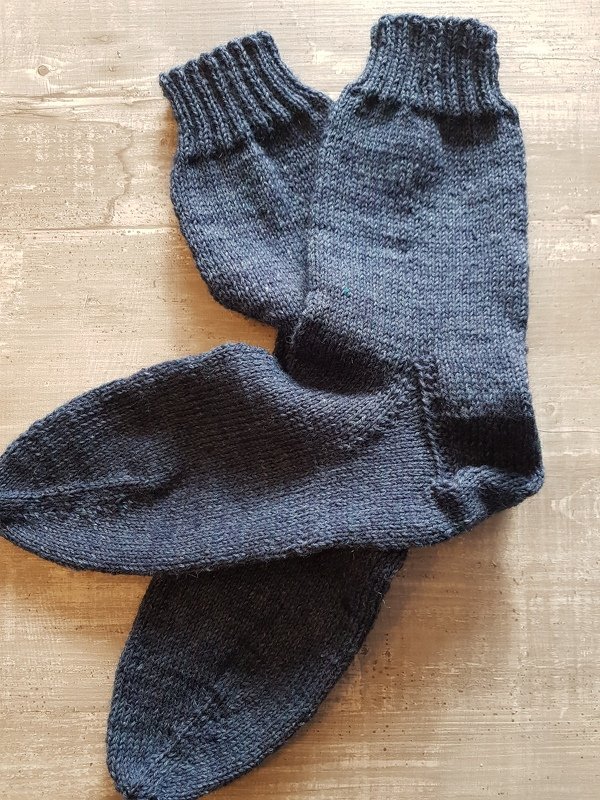 Dunkelgraue, glatt-rechts gestrickte Herrensocken mit Rippenbündchen auf Holzuntergrund
