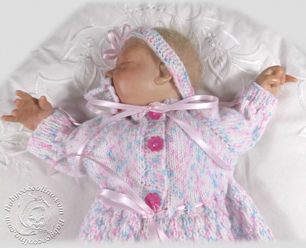 Gestrickte Babyjacke mit Blütenknöpfen, Satinbändern und Stirnband auf Babypuppe