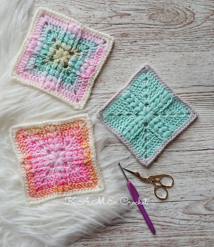Close-up of three pastel textured crochet square swatches with a crochet hook and small embroidery scissors on wood and faux-fur surfaces