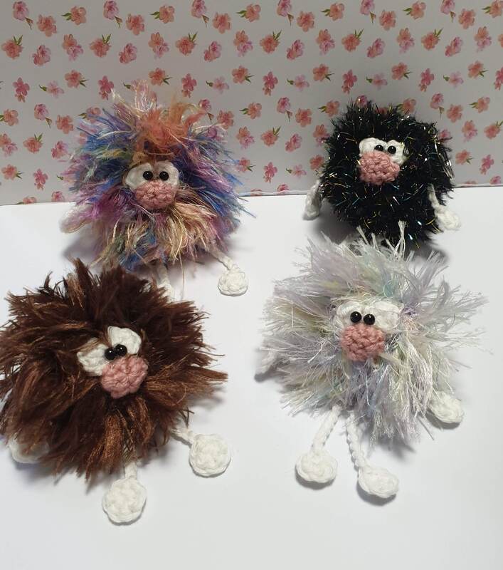 Vier schnell gehäkelte, flauschige Figuren in Regenbogen-, schwarz-, braun- und hellen Tönen mit kleinen weißen Füßen.
