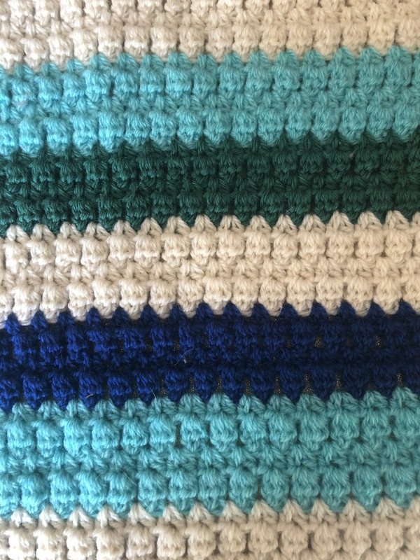 Nahaufnahme gehäkelter Topflappen mit creme-, türkis-, petrol- und marineblauen Streifen