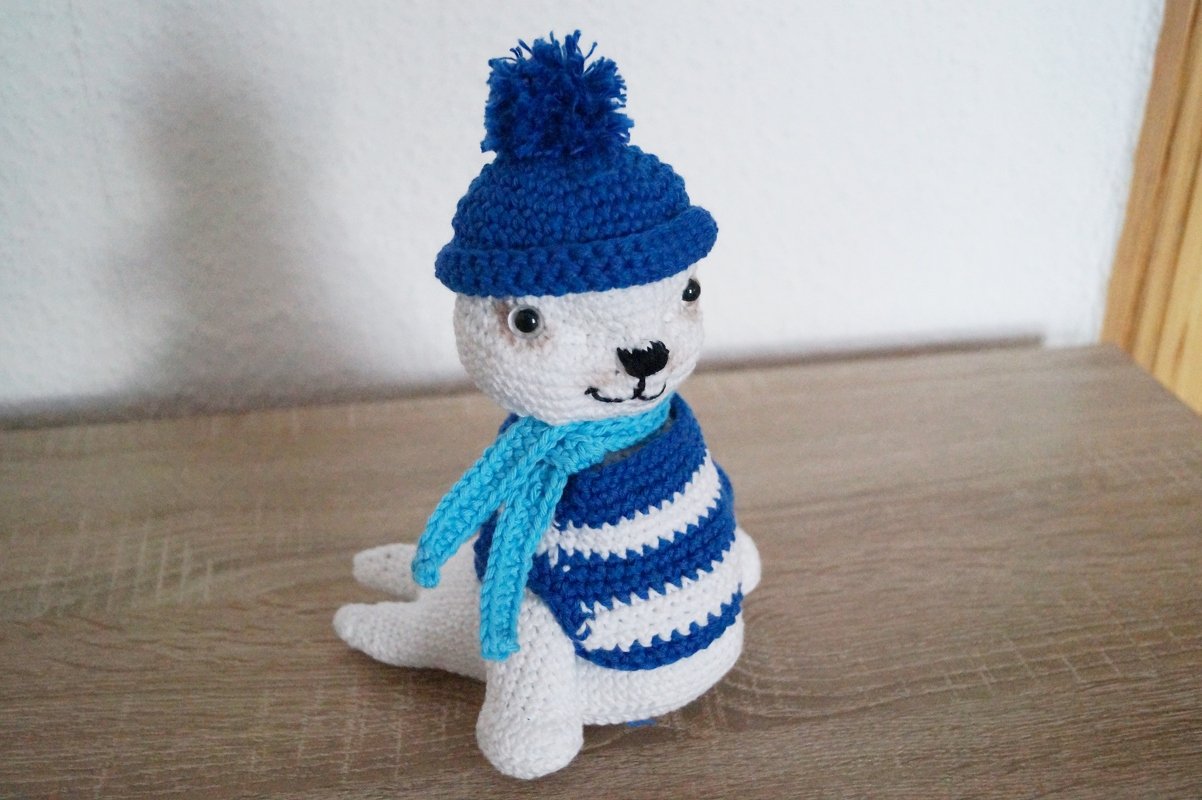 Weiß gehäkelte Amigurumi-Robbe mit blauer Mütze und Schal