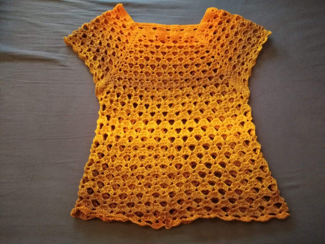 Gehäkeltes gelb-orange Damen-Shirt mit kurzem Ärmel und offenem Lochmuster, flach auf Stoff gelegt