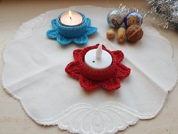 Zwei gehäkelte Blüten-Teelichthalter in Rot und Blau auf weißem Deckchen