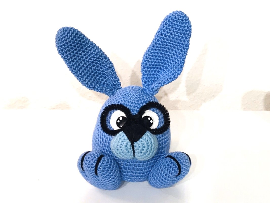Niedlicher gehäkelter blauer Hase mit Brille, großen Ohren und hellblauer Schnauze