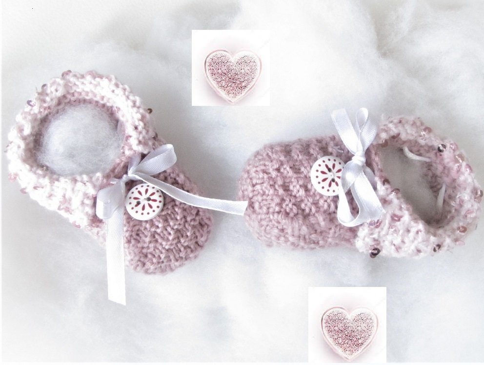 Zwei rosafarbene, handgestrickte Babyschuhe mit Zierschleifen und Knöpfen auf weichem Untergrund