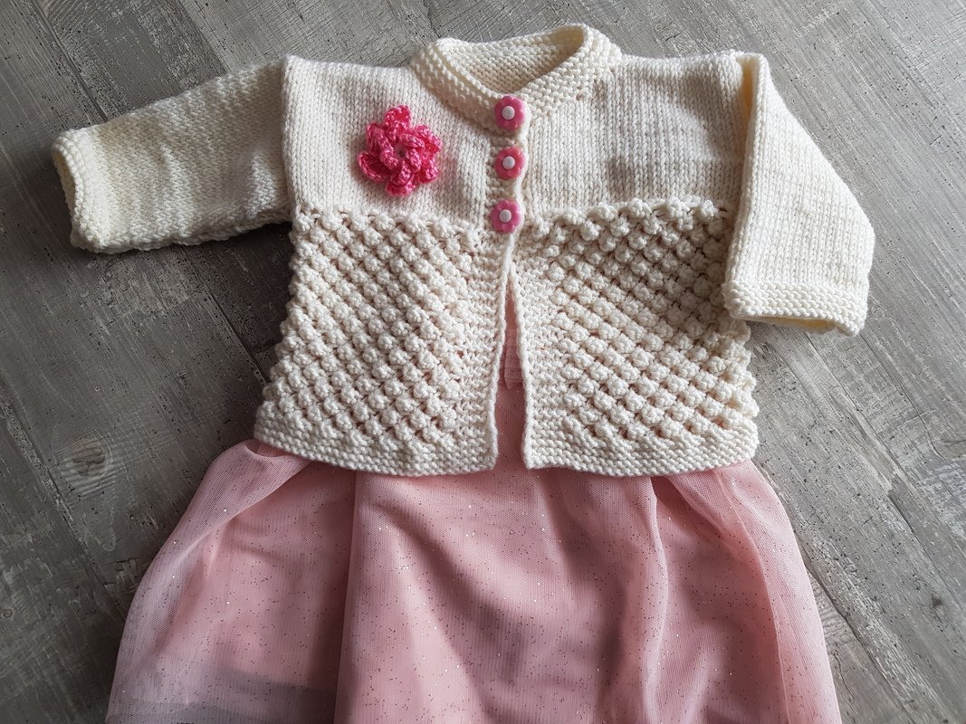 Festliches Baby-Outfit mit cremefarbener Strickjacke, blütenförmigen rosa Knöpfen und rosa Tüllkleid