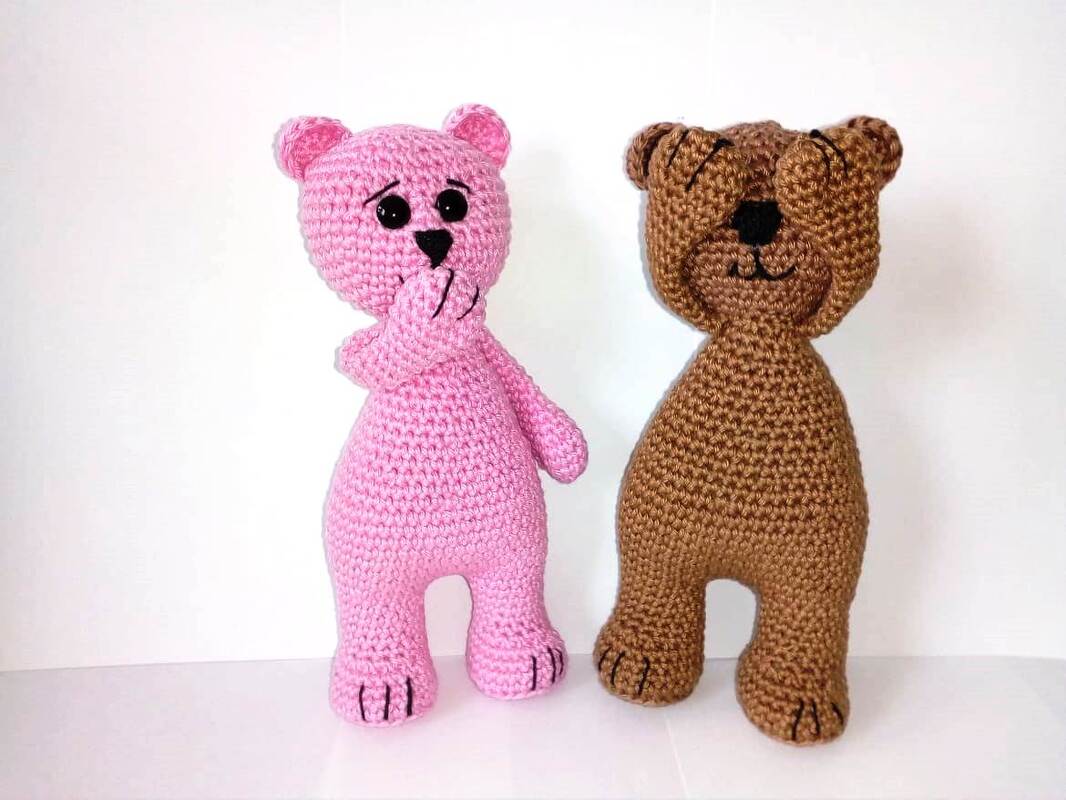 Zwei gehäkelte Amigurumi-Teddys (rosa und braun); rosa hält Hand vor Mund, braun bedeckt die Augen; weißer Hintergrund.