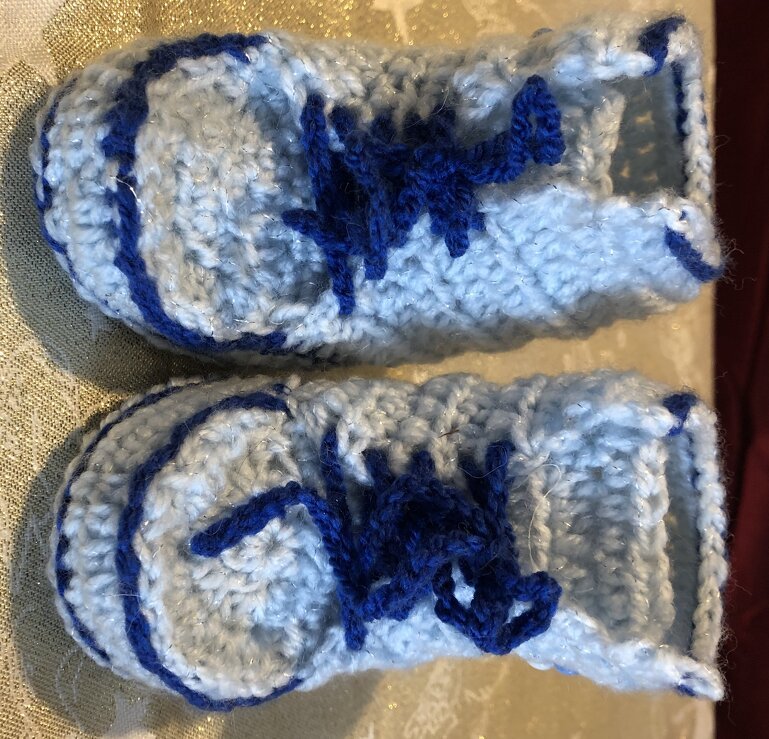 Ein Paar handgehäkelter hellblauer Baby-Booties mit dunkelblauer Zierschnürung, von oben fotografiert.