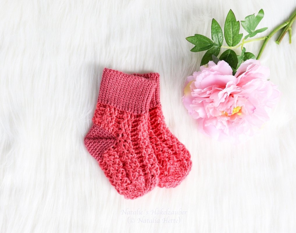 Korallrosa gehäkelte Babysocken mit Rippbündchen und Ajourmuster auf weißem Fell