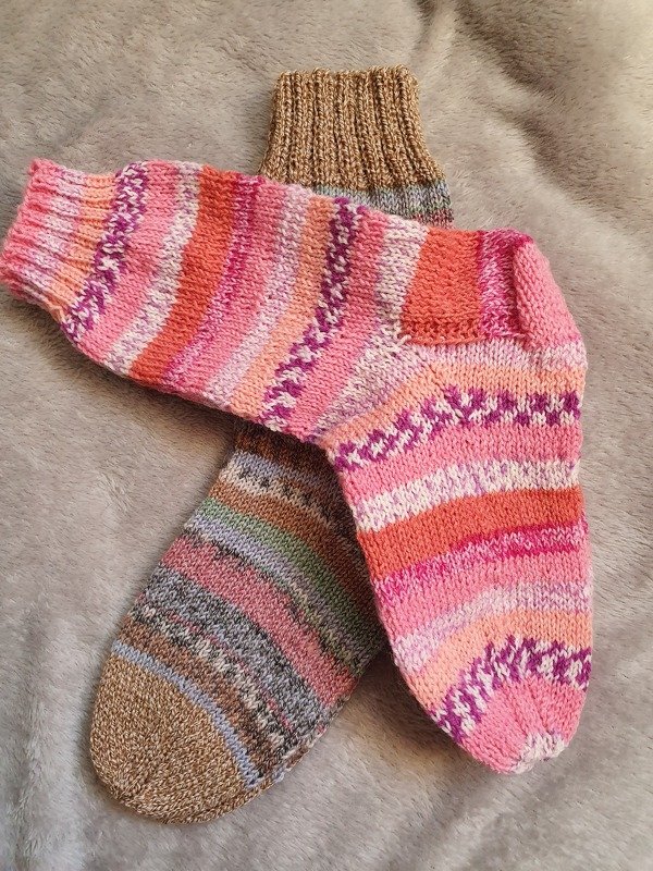 Handgestricktes Paar Damensocken mit buntem Streifenmuster, übereinander liegend auf grauem Stoff