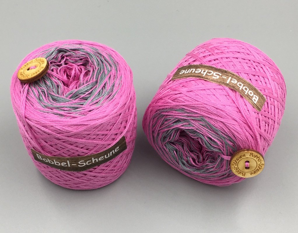 Zwei pink-graue Bobbel-Garne mit Holzknöpfen auf grauem Hintergrund