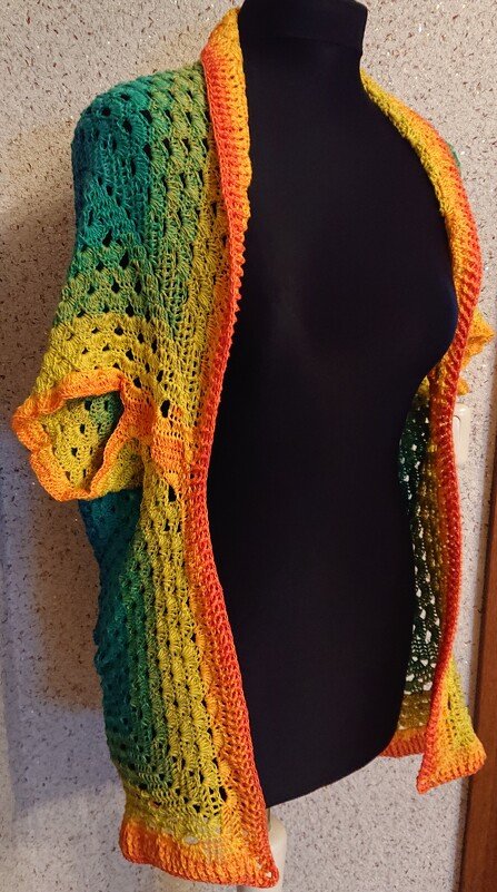 Gehäkelte Damenweste in Grün, Gelb und Orange mit Ajourmuster und kurzen Ärmeln auf einer schwarzen Schneiderbüste.