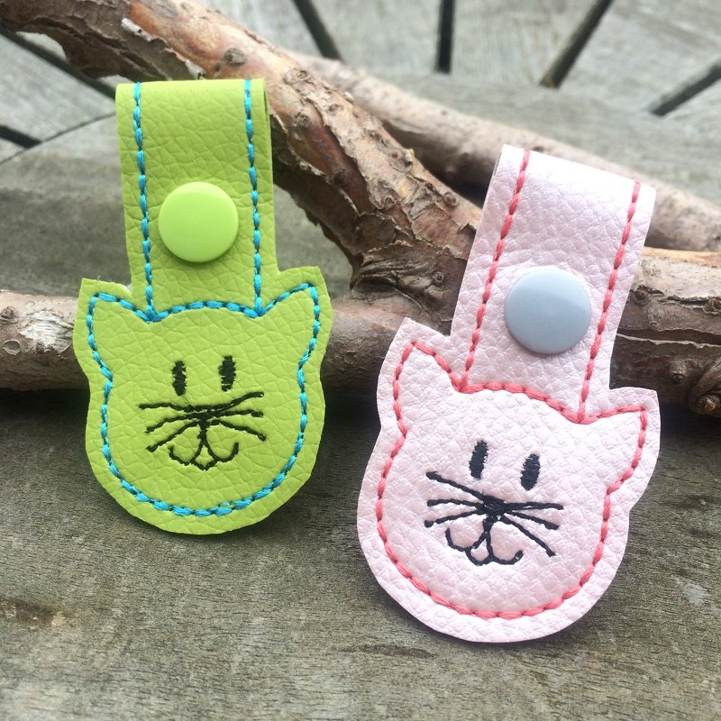 Zwei ITH-Schlüsselanhänger in Katzenform aus Kunstleder, grün und rosa, mit gesticktem Katzengesicht und Druckknopfriemen