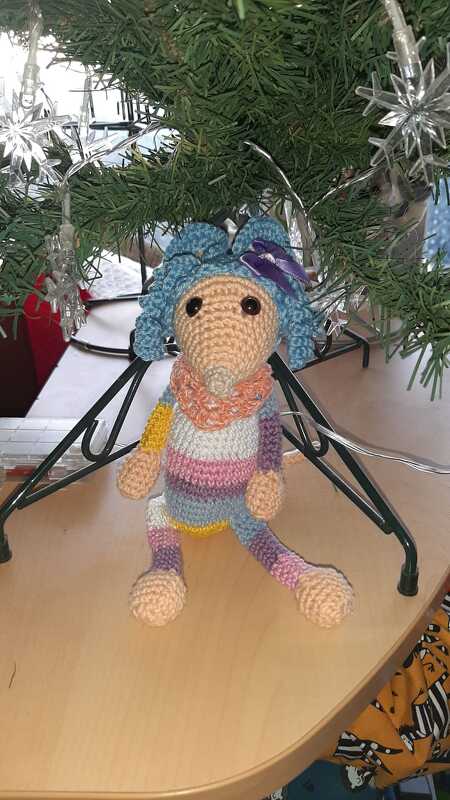 Gehäkelte Amigurumi‑Maus mit blauen Locken, orangefarbenem Schal und gestreiftem Körper