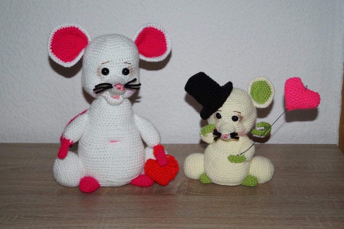 Zwei gehäkelte Amigurumi‑Mäuse: weiße mit rotem Herz, cremefarbene mit Zylinder und Herzballon.