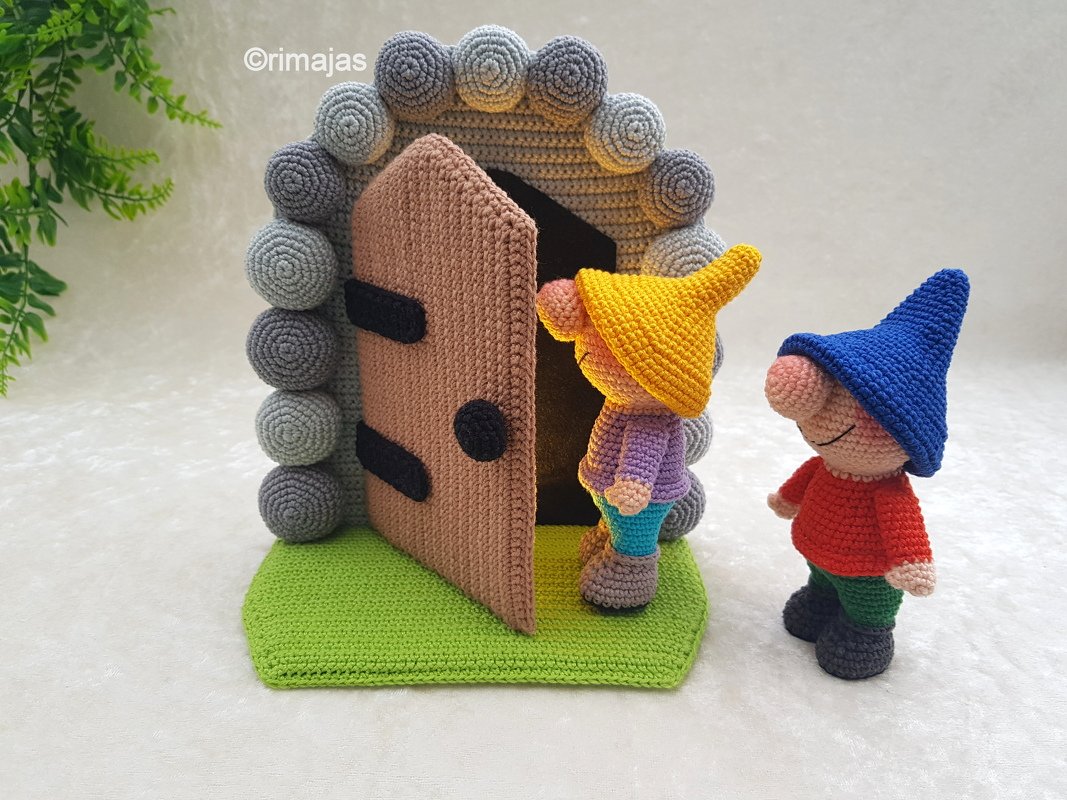 Zwei gehäkelte Wichtel vor einer offenen braunen Rundtür mit grauem Kugelrahmen auf grünem Untergrund