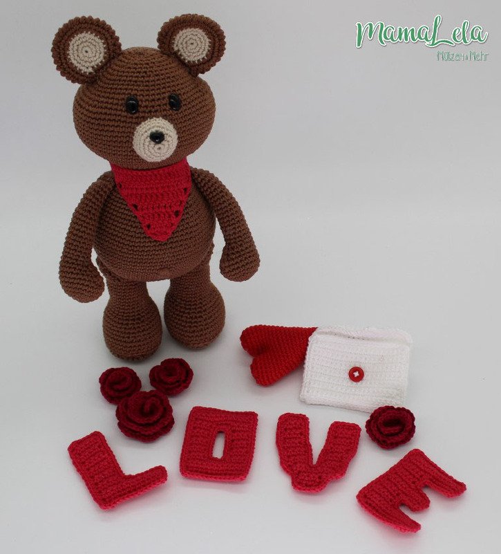 Brauner Häkel-Teddy mit rotem Dreieckstuch, gehäkelte Buchstaben 'LOVE', rote Rosen und weißer Umschlag