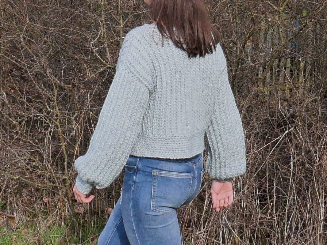 Person von hinten in mintgrünem, gehäkeltem Kurzpullover mit weiten Ärmeln und blauen Jeans.