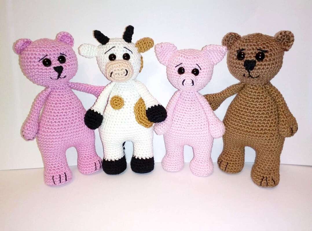 Vier gehäkelte Amigurumi-Tiere nebeneinander: rosa Bär, weiße Kuh mit braunen Flecken, hellrosa Schwein und brauner Bär