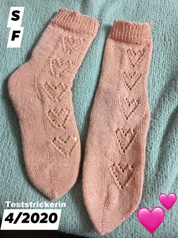 Nahaufnahme eines Paar rosafarbener Socken mit vertikalem Herz-Lochmuster, Rippenbündchen und glatt rechts gestrickter Fläche