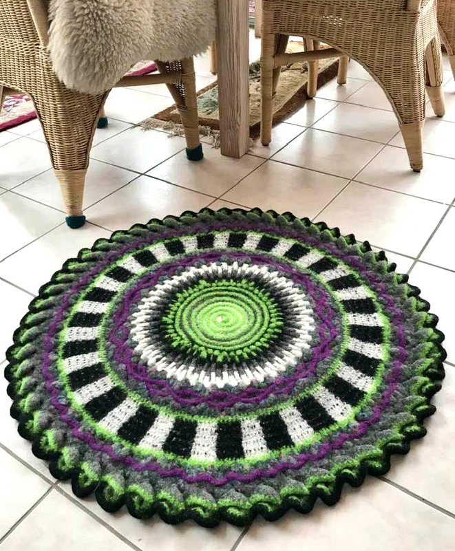 Runder gehäkelter und gefilzter Teppich in Grün, Lila, Schwarz und Weiß auf Fliesenboden neben Korbstühlen