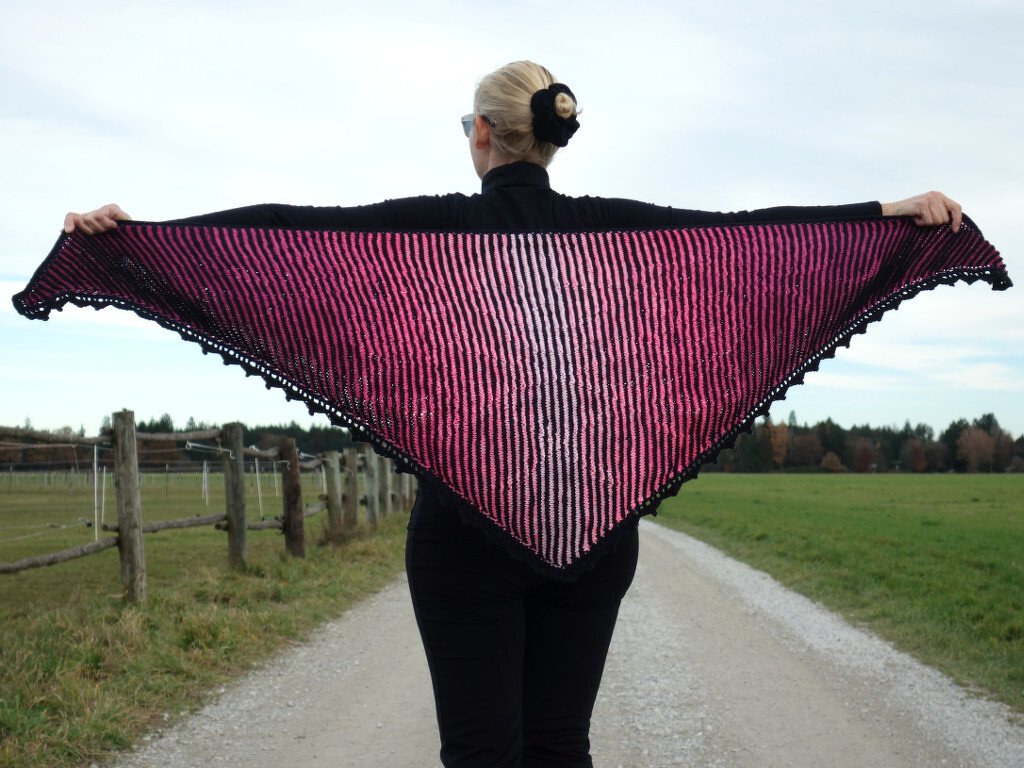 Geöffnete Ansicht eines gestrickten Dreieckstuchs mit Streifenmuster und Lochkante, gehalten von einer Person von hinten