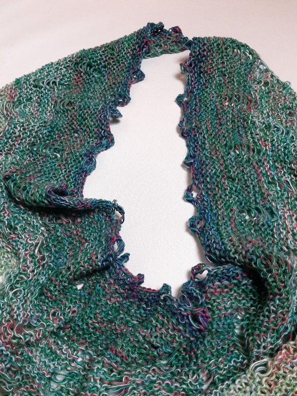 Nahaufnahme eines gestrickten Dreieckstuchs in Grün- und Blautönen mit offener Struktur und Schlaufenkante