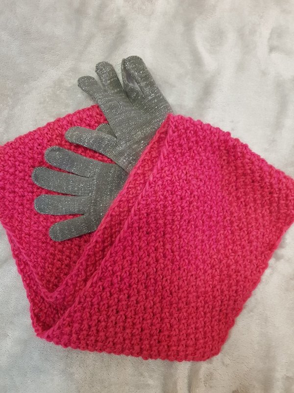 Gestrickter fuchsiafarbener Loopschal und graue Glitzerhandschuhe auf weißer Decke
