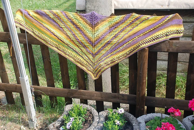 Dreieckiges gestricktes Tuch in Gelb, Grün und Lila auf einem Holzzaun