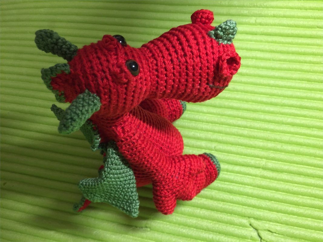 Rot-grüner gehäkelter Amigurumi-Drache mit Flügeln auf grünem Hintergrund