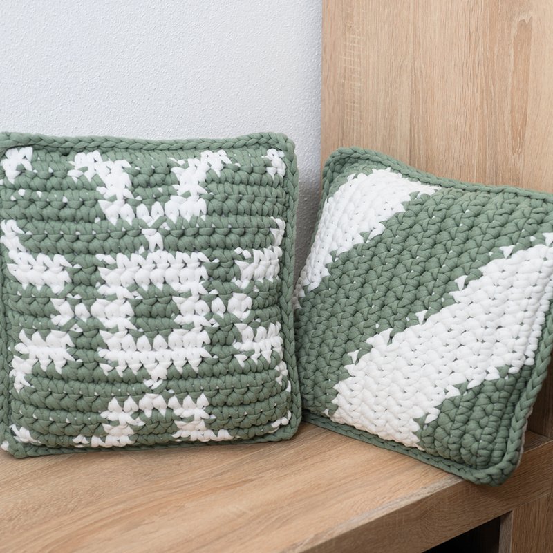 Zwei gehäkelte Kissenbezüge in Grün und Weiß auf einer Holzbank