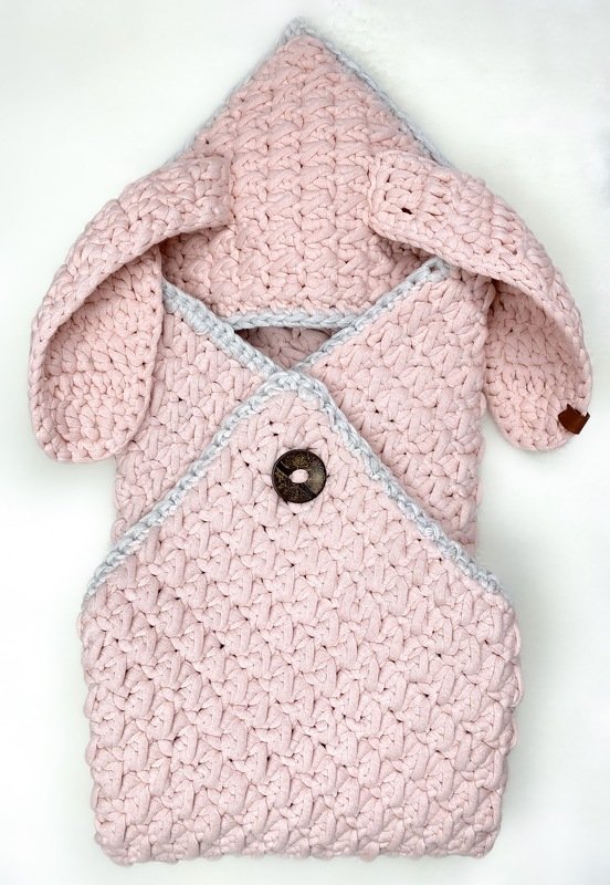 Rosa gehäkelter Babyschlafsack mit Hasenohren und Holzknopf auf weißem Hintergrund.