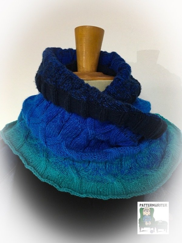 Gestrickter Loop-Schal in Blau- bis Türkistönen mit Zopfmuster auf einer Schaufensterpuppe